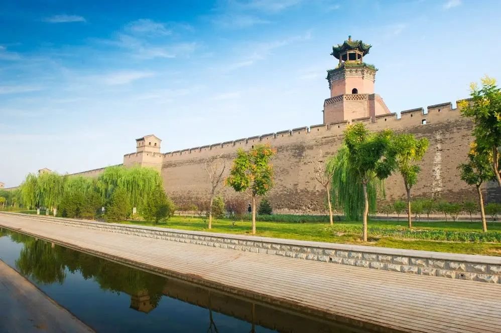 Pingyao’s city wall, watchtower and green moat-side promenade beneath a blue sky.