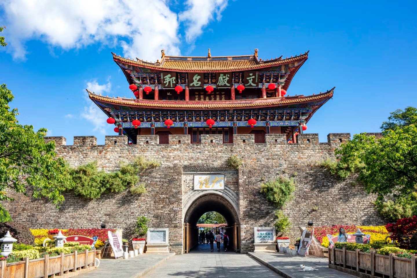 Dali Old Town’s South Gate in bright daylight, with red lanterns, stone ramparts and a clear blue sky.
