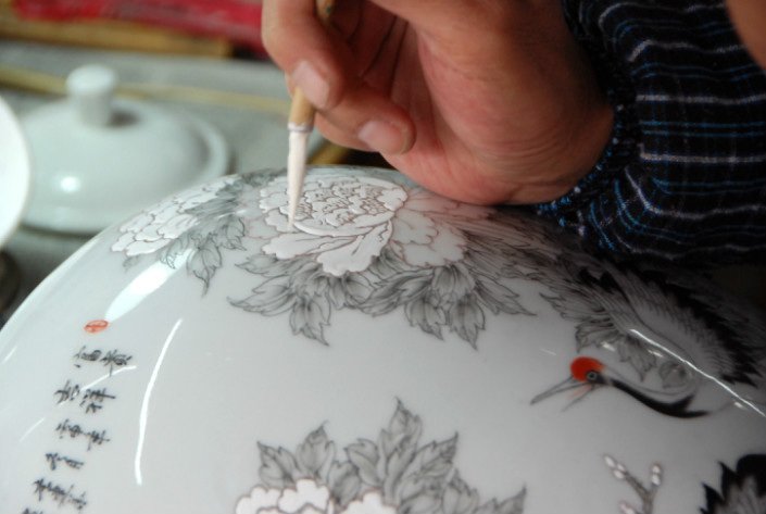 A Jingdezhen artisan uses a fine brush to decorate a porcelain bowl with floral motifs.