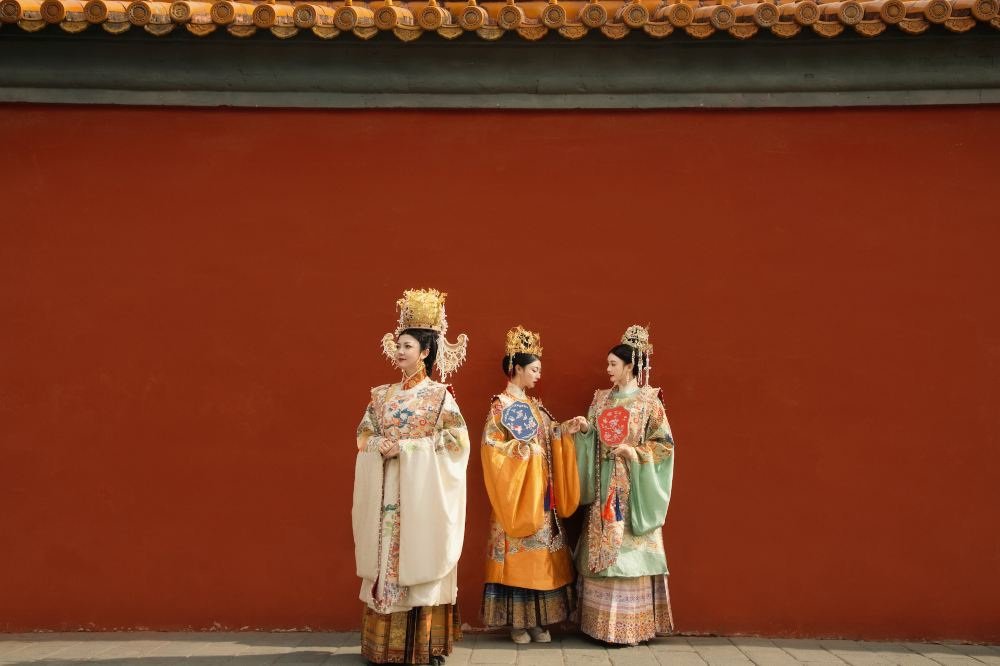 Elaborate embroidered hanfu-inspired dress and formal hair ornaments in a styled palace-wall photoshoot.