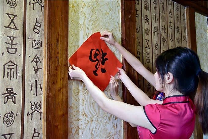 A woman places an upside-down fu decoration on a wooden doorway for Spring Festival.