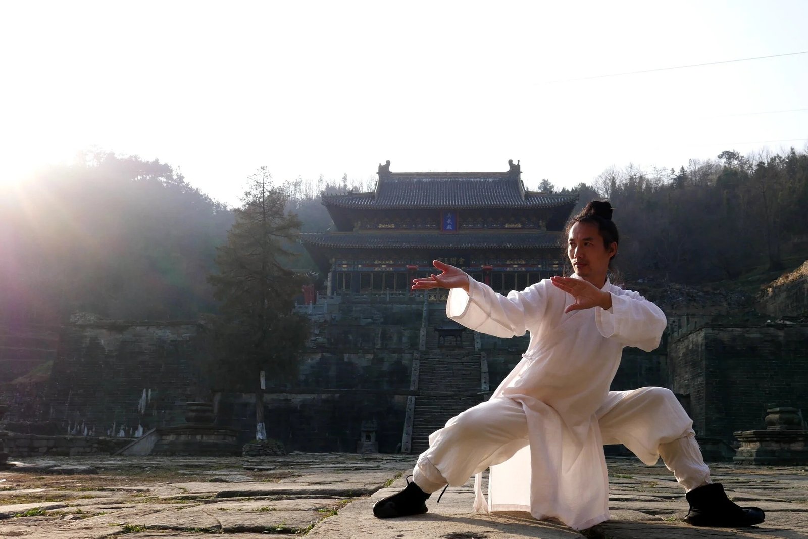 A white-robed practitioner demonstrates Wudang-style tai chi in a temple courtyard