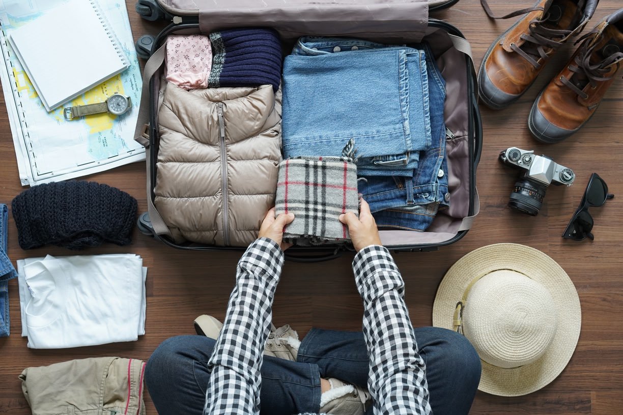 A traveler arranges folded clothes and essentials in an open suitcase.