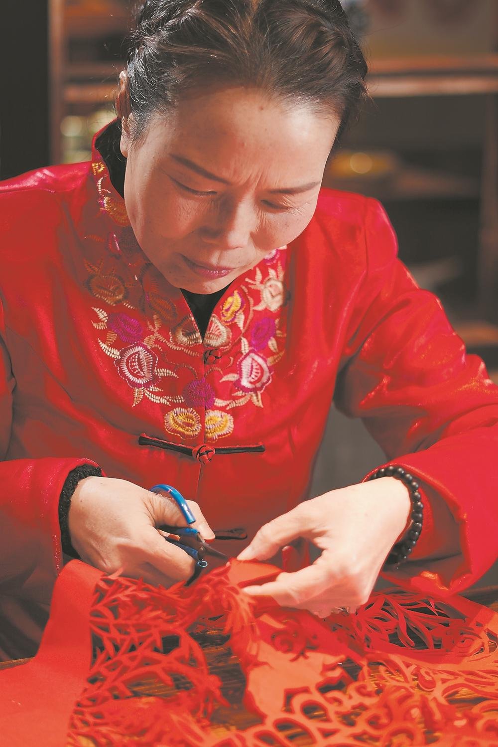 A Zherong paper-cutting artisan guides small scissors through an intricate red paper design