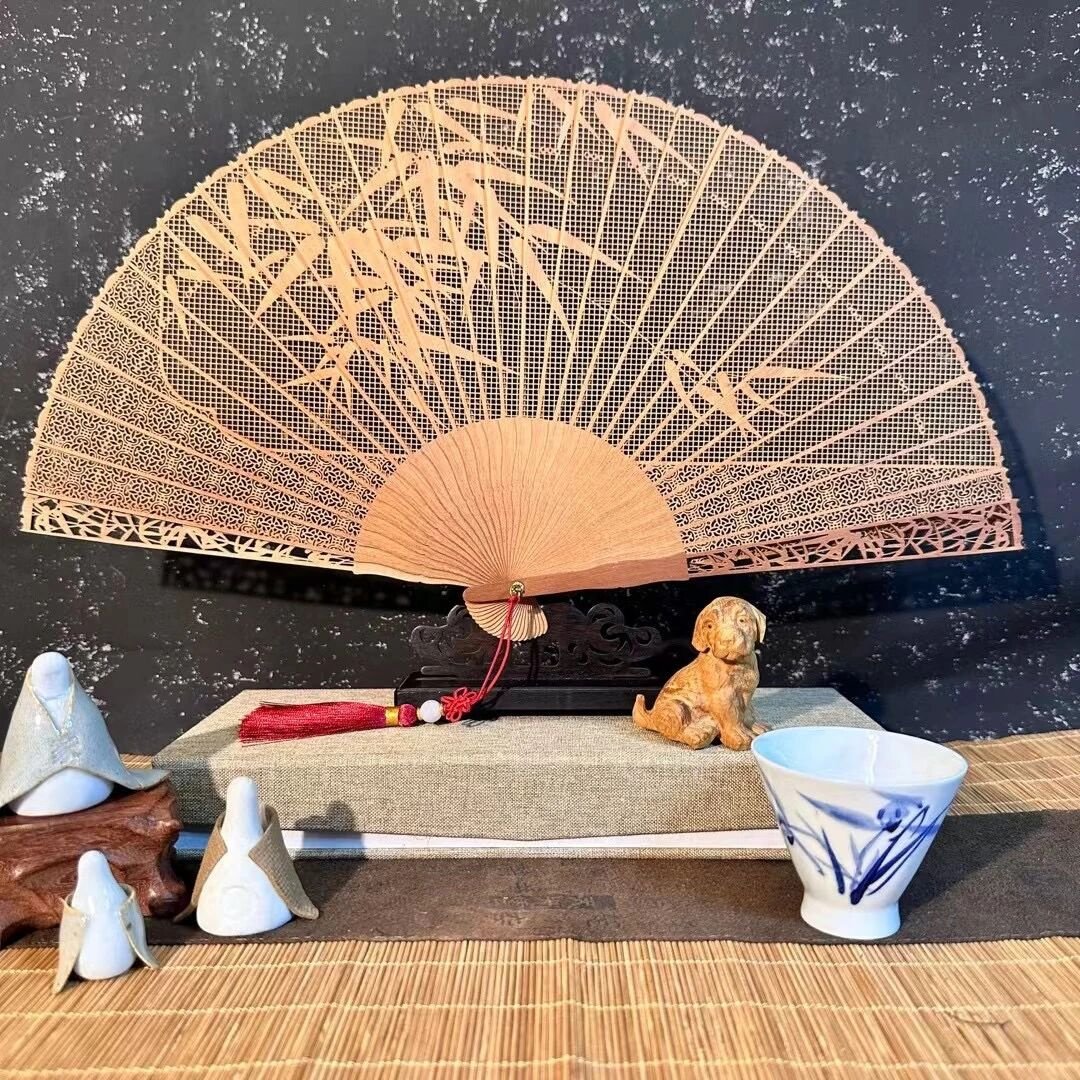 Open pierced wooden folding fan with bamboo motifs, displayed beside blue-and-white ceramics