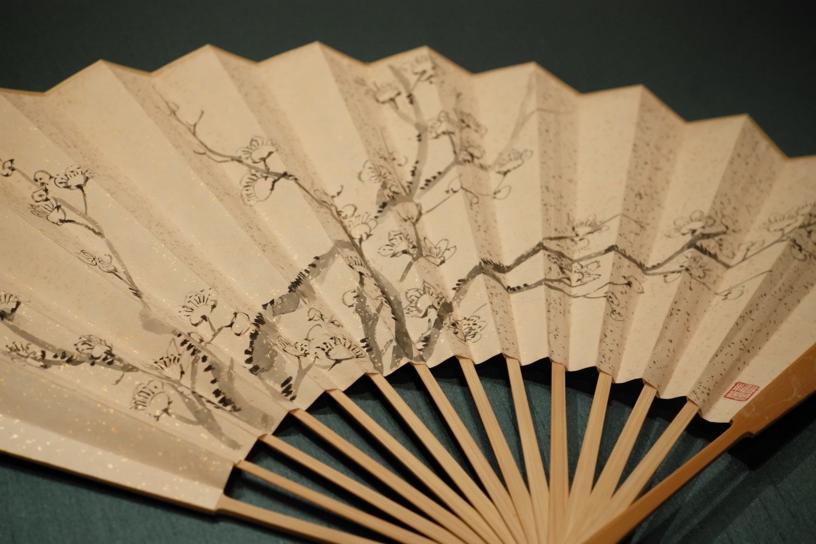 Plum blossoms, calligraphy and red seals across the pleats of a paper folding fan
