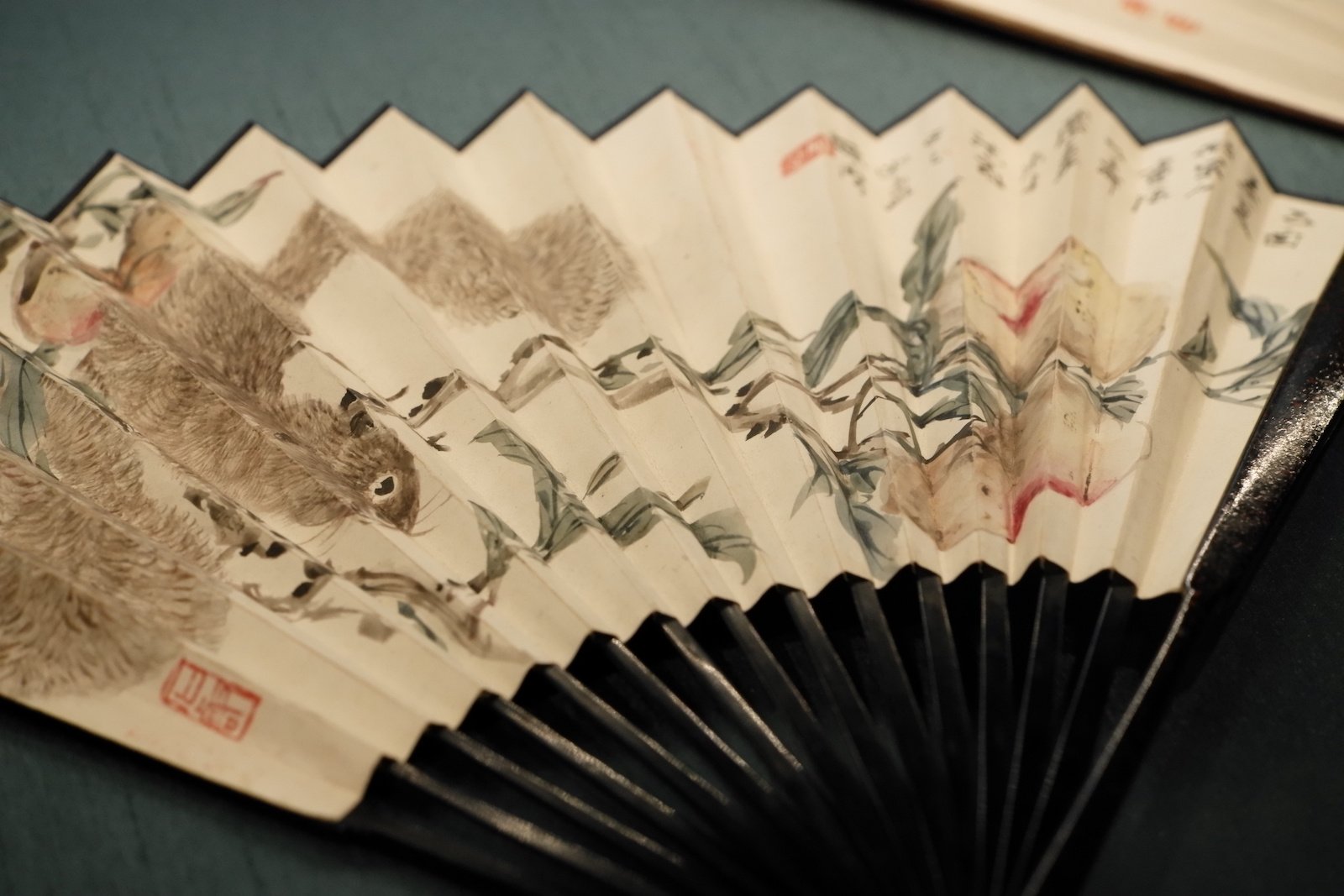 Detail of a squirrel and pomegranates painted across a folding fan with dark ribs